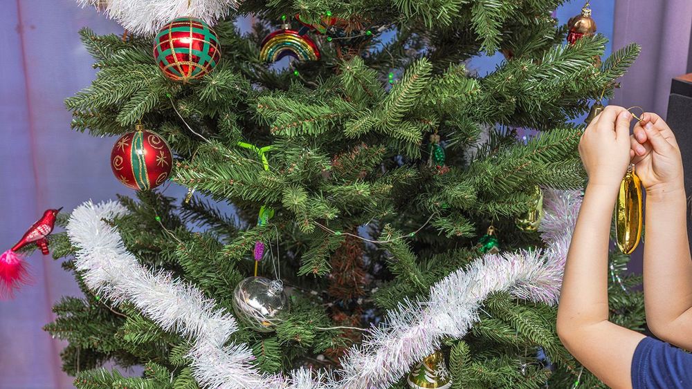 Child hanging golden ornament on beautifully decorated Christmas
