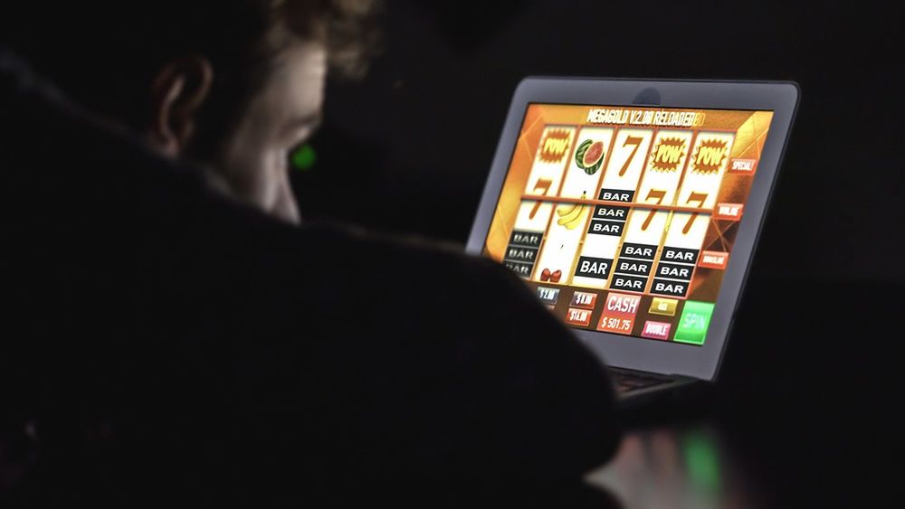 Gambling addicted man in front of online casino slot machine on laptop computer at night.