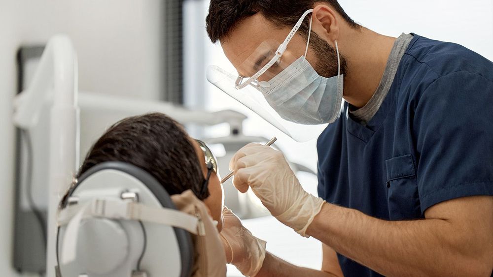 Young Adult Male Dentist Examining Patient during Dental Appointment