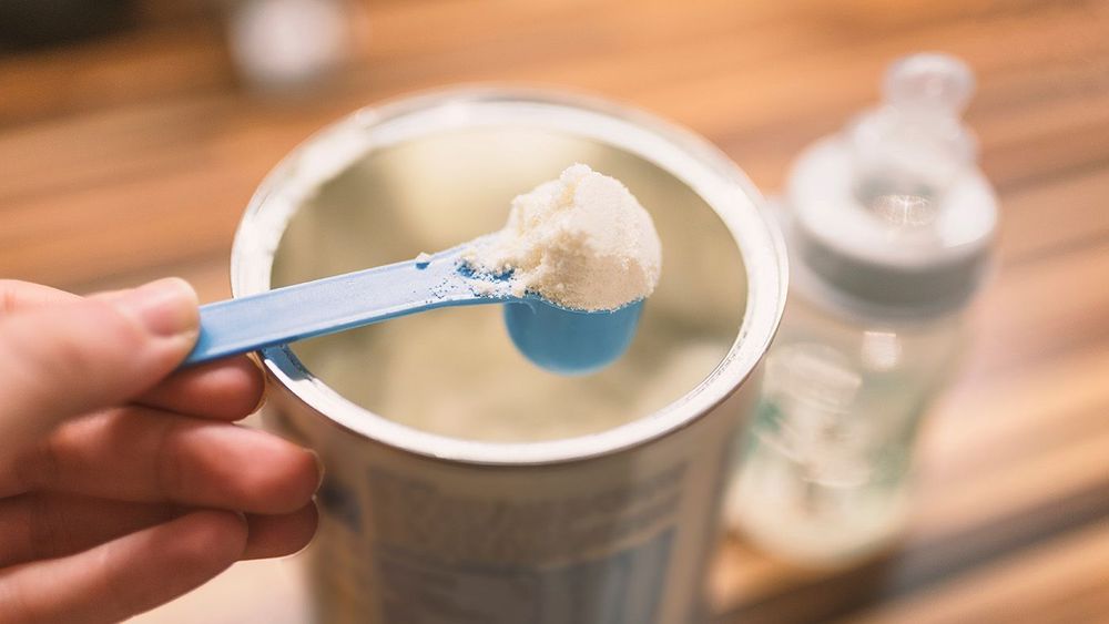 Powder milk for baby and blue spoon on light background close-up