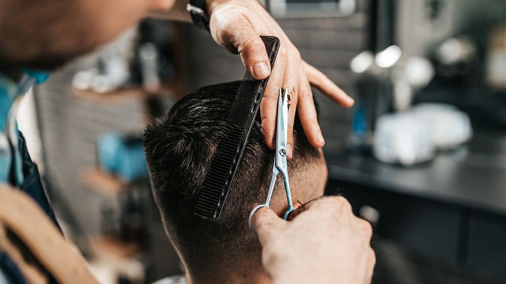 Good looking bearded man visiting hairstylist in barber shop.