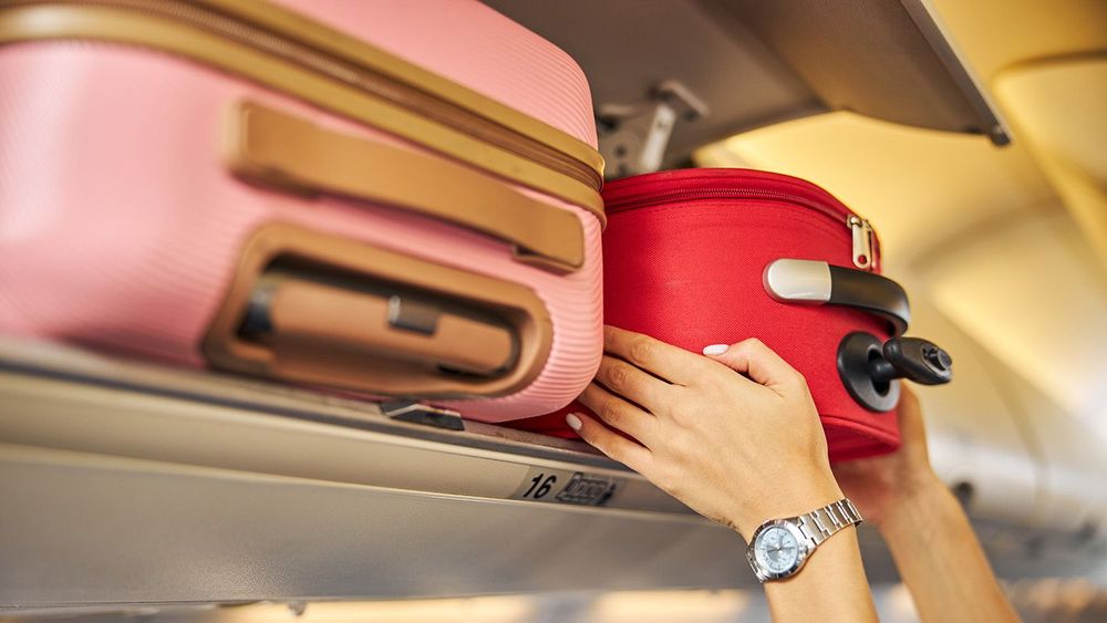 Hands laying down a carry-on baggage on an upper shelf