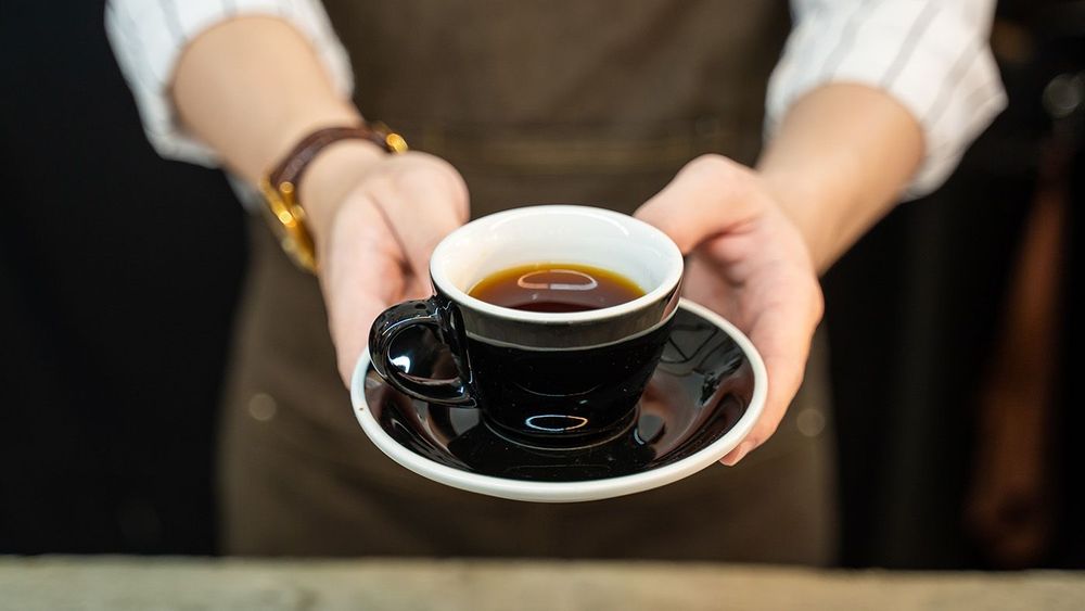 Close-up shot of barista serving hot coffee to customer in coffe