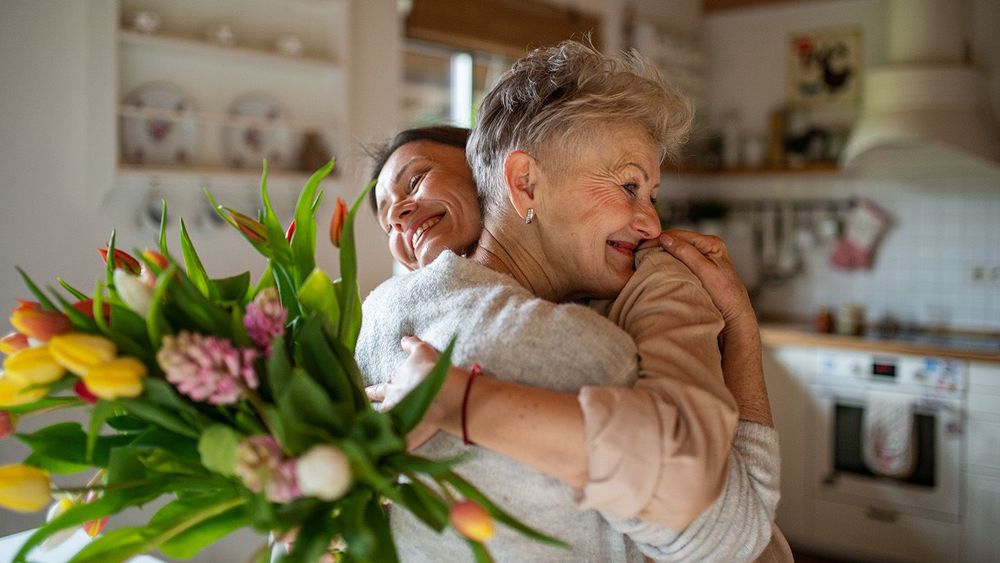 Happy senior mother hugging adult daughter indoors at home, mothers day or birthday celebration.