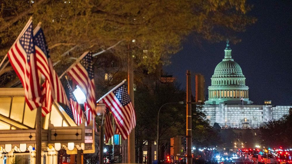 Night time view of the US Capitol seen from Pennsylvania Avenue downtown with American flags in Washington DC USA