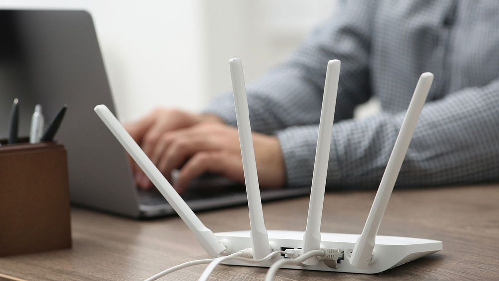 Man with laptop working at wooden table indoors, focus of Wi-Fi