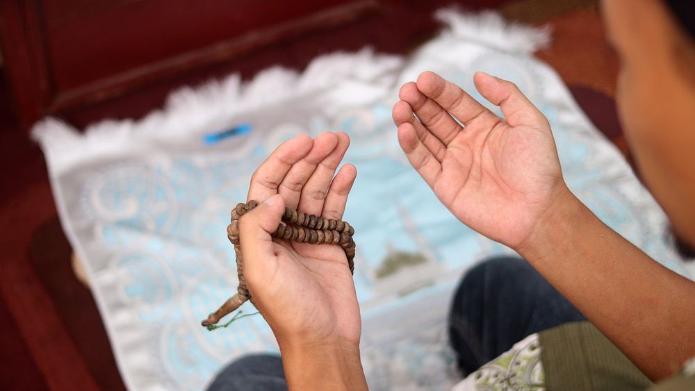 On a prayer mat at home, an Indonesian man raises open palms in
