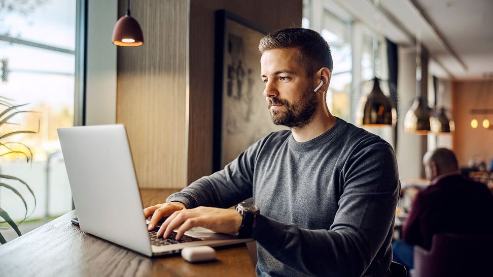 A freelancer is sitting at cafeteria and typing report on a lapt
