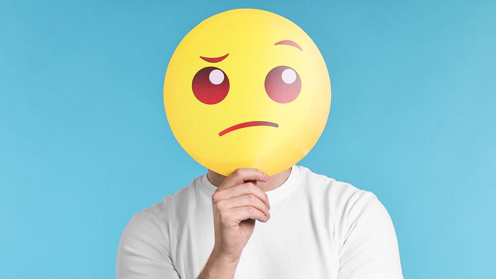 Man covering face with thinking emoticon on light blue backgroun
